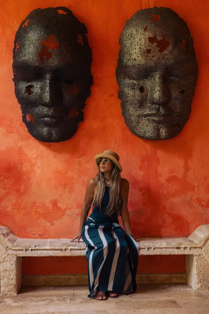 Huésped sentada bajo dos máscaras de la colección de arte sobre un muro de color terracota